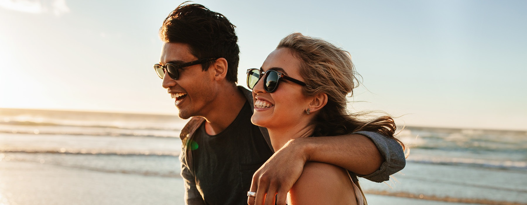 a young couple wearing sunglasses, walk along a beach