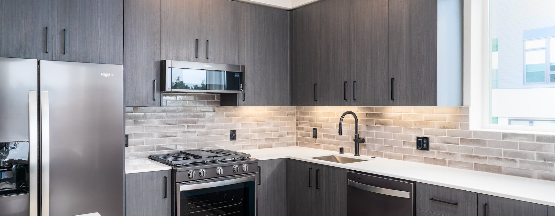 Santa Clara, CA, Apartments - Sofia - Kitchen with Stainless Steel Appliances, Italian Cabinetry, Hardwood Style Flooring, Quartz Countertops, Tile Backsplash, and a Window.