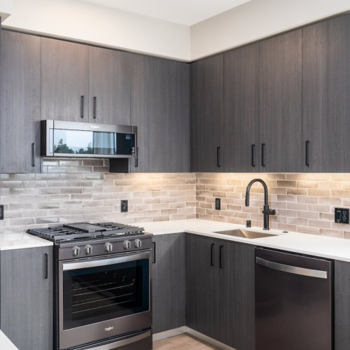 Well-lit kitchen with ample counter space Santa Clara, CA, Apartments - Sofia - Kitchen with Stainless Steel Appliances, Italian Cabinetry, Hardwood Style Flooring, Quartz Countertops, Tile Backsplash, and a Window.
